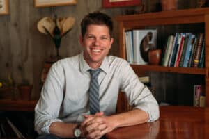An image of the author, Matt Ritter, sitting at a desk, wearing a dress shirt and tie, smiling. 